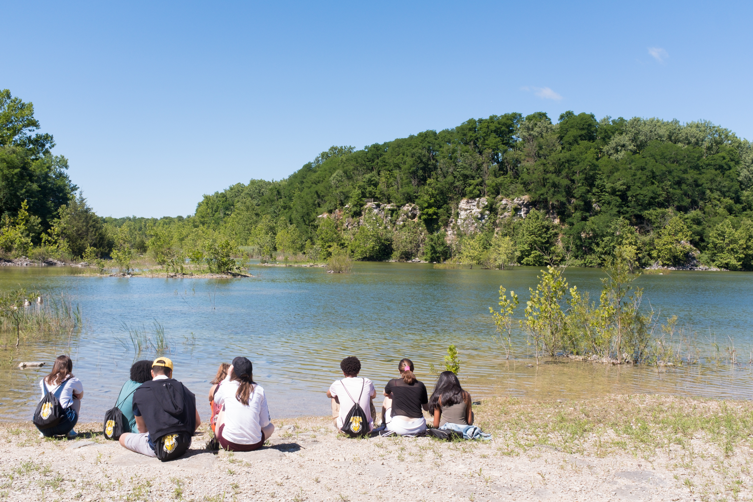 ISHIP students sitting at the shore of a lake, staring out at the forest on the other side.